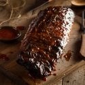 Ribs on a cutting board with sauce and knife.